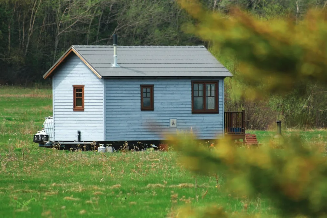 Tiny house en bois peint en bleu clair posée sur ses roues au milieu d'une prairie