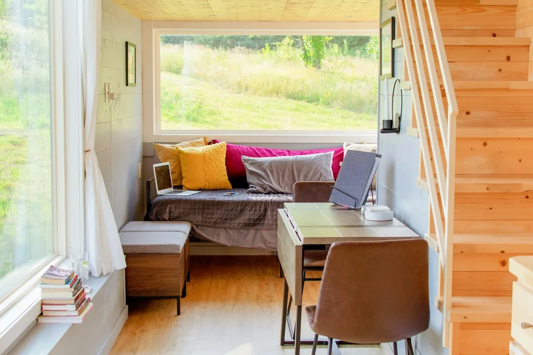 Intérieur d'une tiny house avec banquette, coin bureau et escalier en bois vers la mezzanine